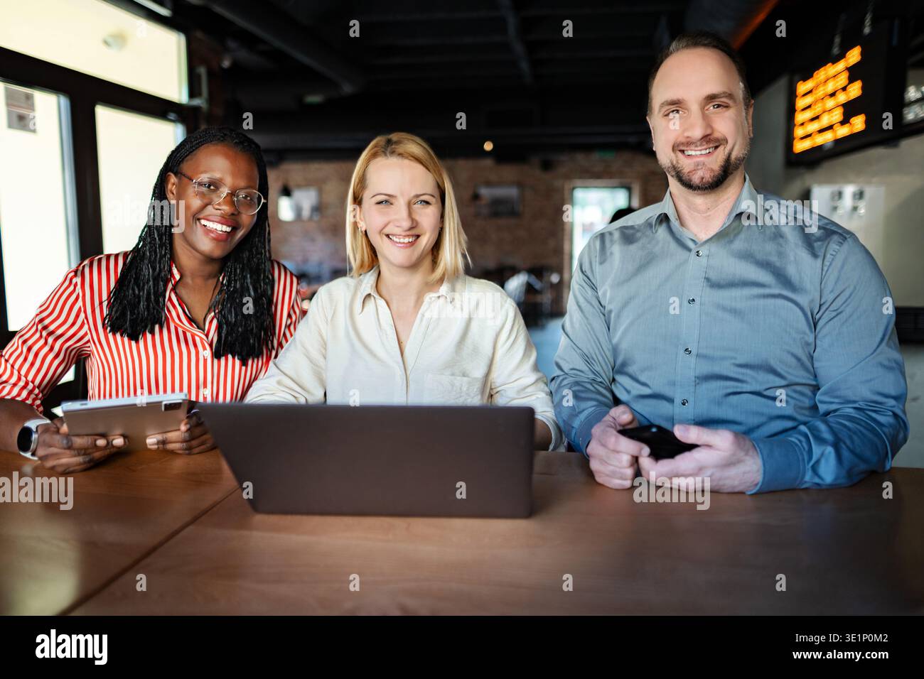 Diverse business team collaborating using technology smiling for camera Stock Photo