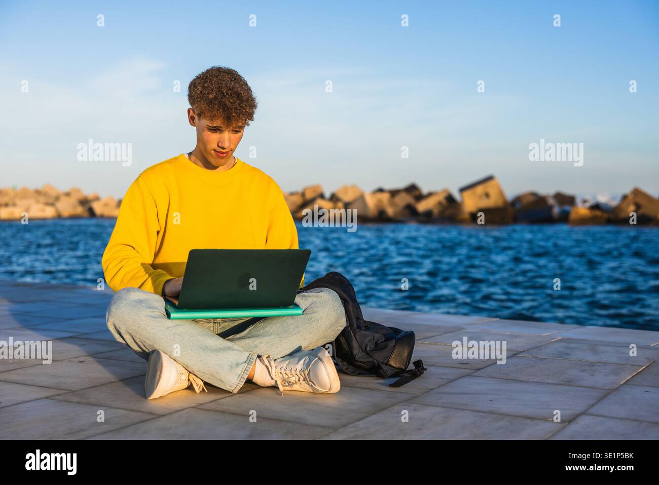 College student working on laptop by the sea at sunset Stock Photo