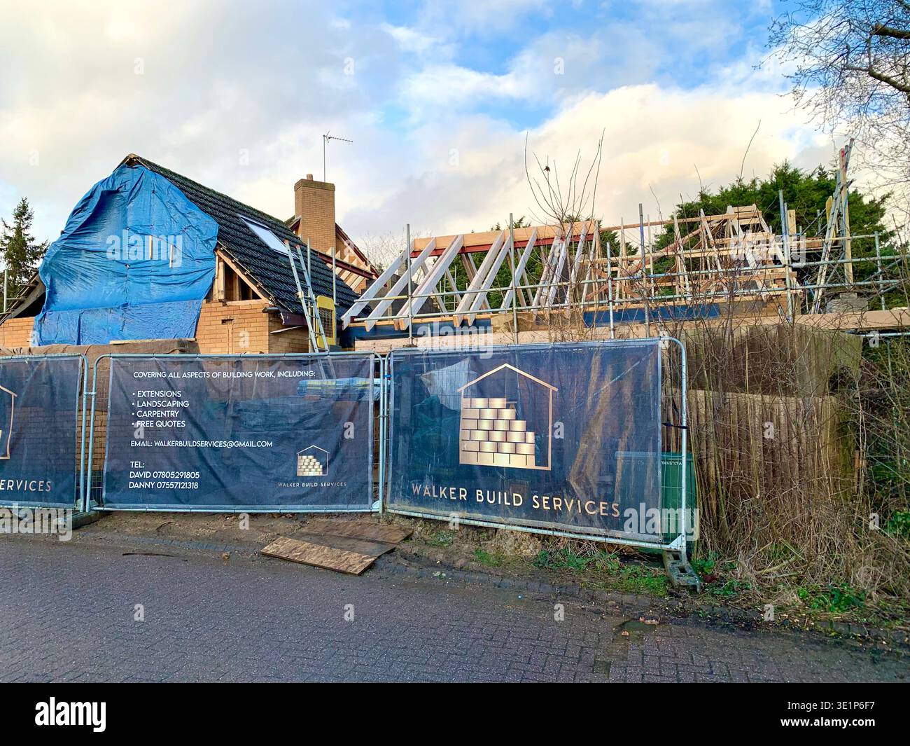 Residential renovation in progress on a suburban street with one house undergoing roof repairs under a blue tarp and another showing exposed timber - Smartphone Captured Stock Image