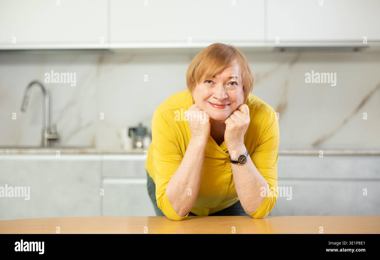 Happy older lady standing in kitchen with warm smile Stock Photo