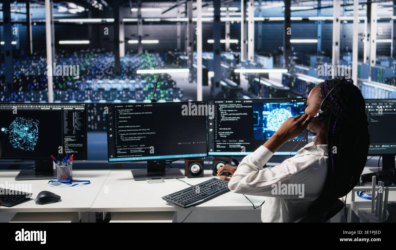 System administrator in data center wearing headset assisting users with artificial intelligence troubleshooting. IT expert in server farm managing support tickets using machine learning, camera A Stock Photo