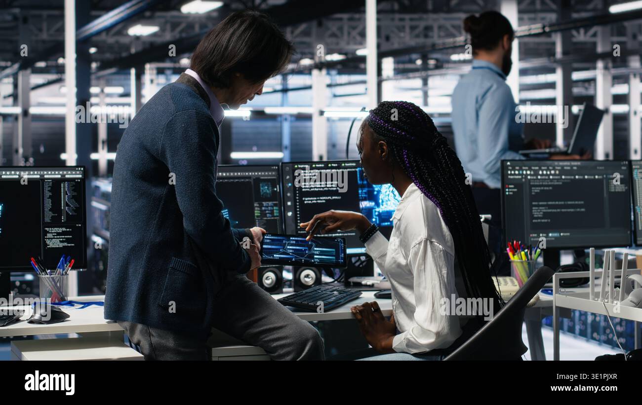 Senior engineer and trainee in data center working on neural network software development. Lead programmer and intern in server room implementing machine learning technology using PC, camera A Stock Photo