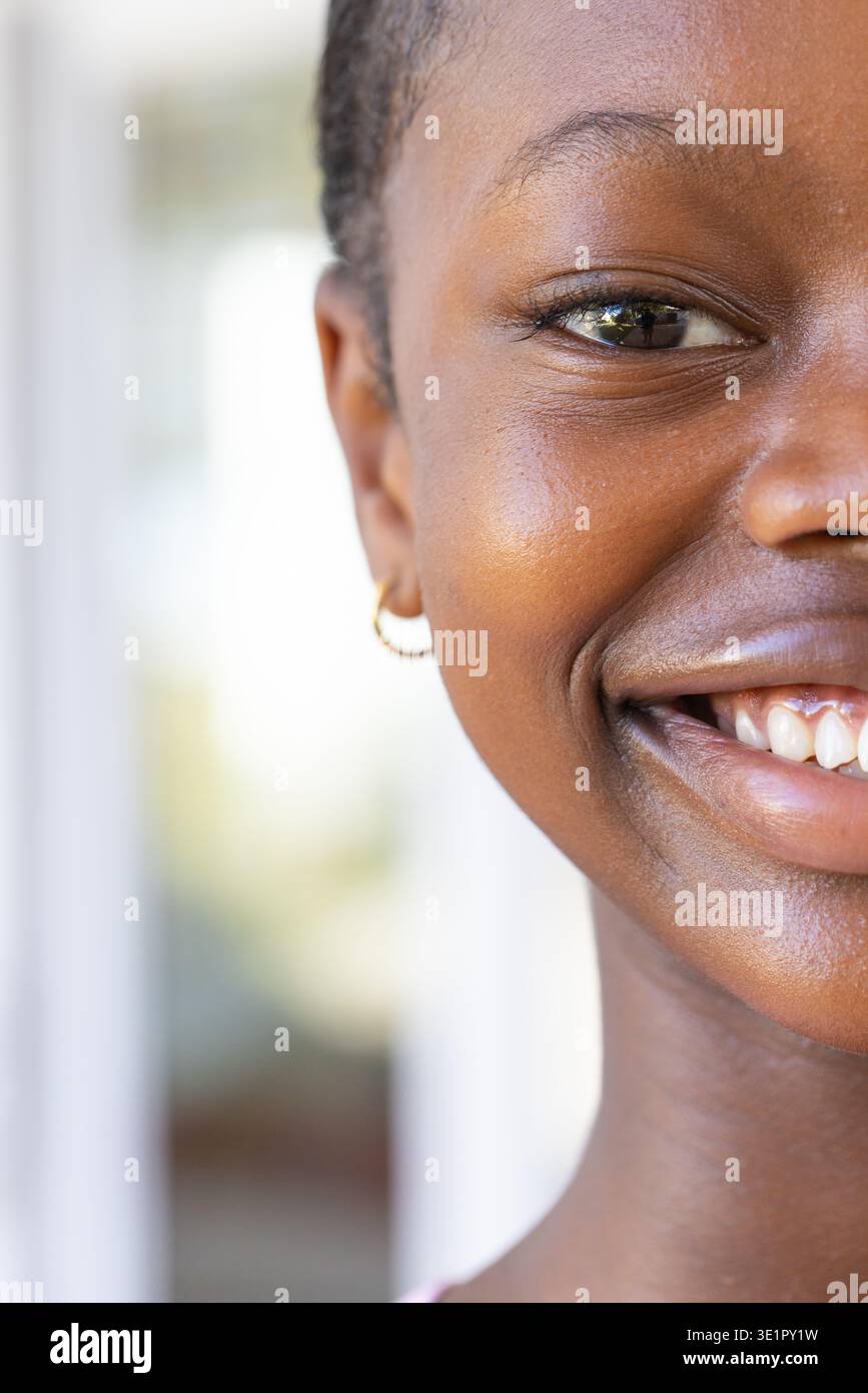 african-adolescent-female-smiling-with-teeth-facing-camera-by-bright-window-with-gold-hoop-earring-3E1PY1W.jpg