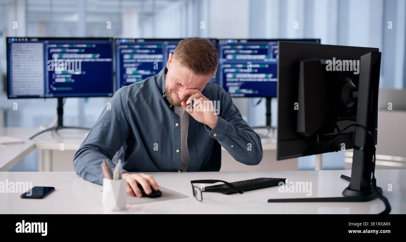 Tired Programmer Rubs Irritated Eye During Long Coding Session At Desk Stock Photo