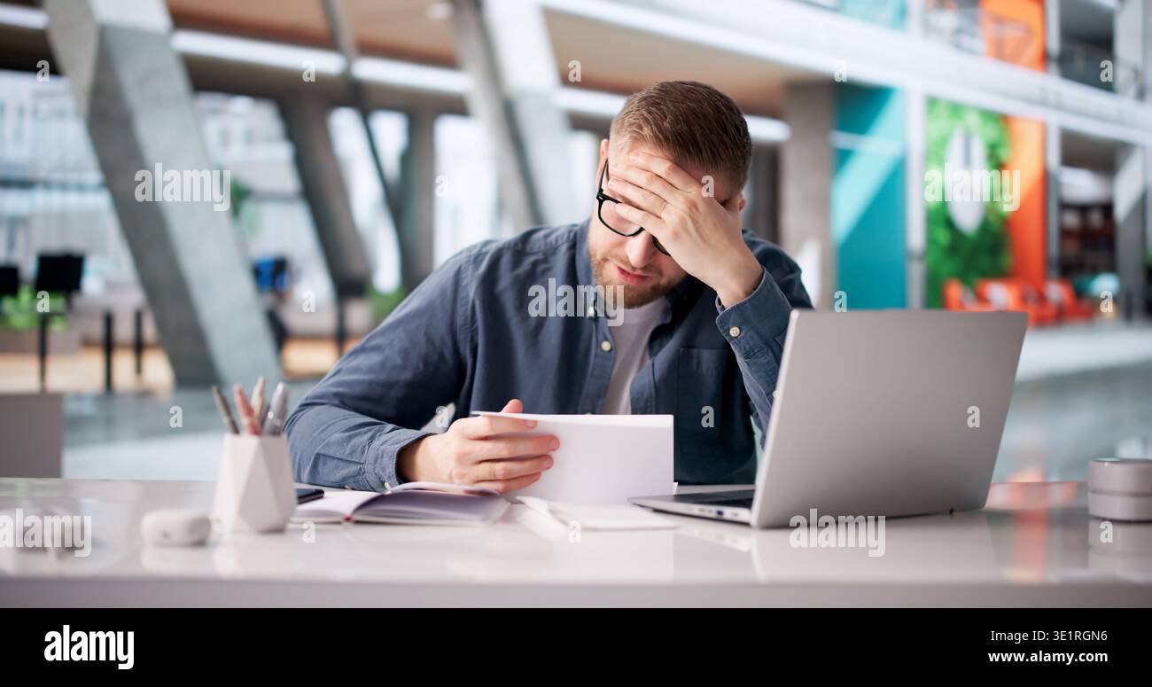 Stressed Young Man Reacting To Troubling Document At Workstation Stock Photo