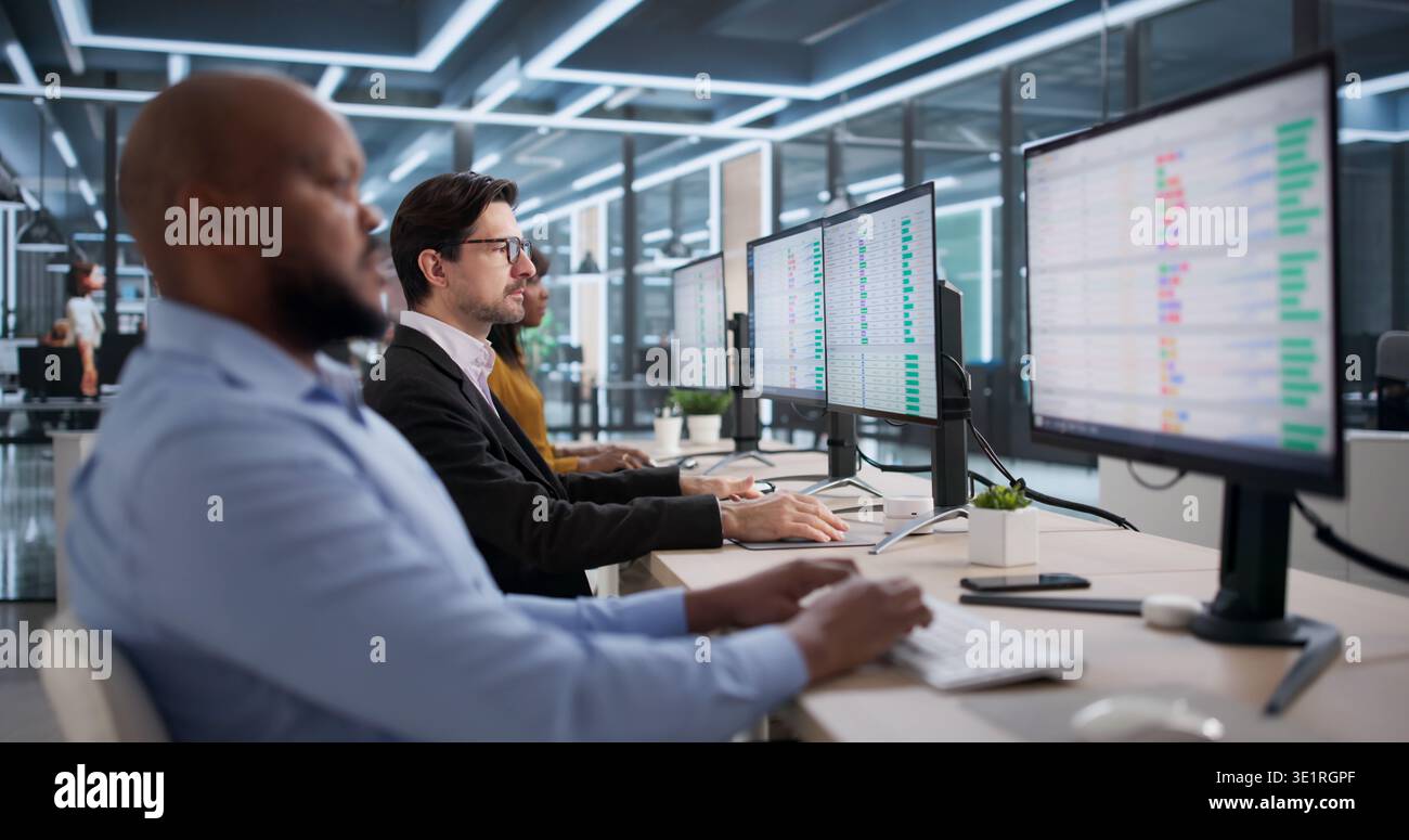 Diverse Team Of Professionals Using Spreadsheets On Desktop Computers Happily. Man And Woman Analysts Studying Reports Stock Photo