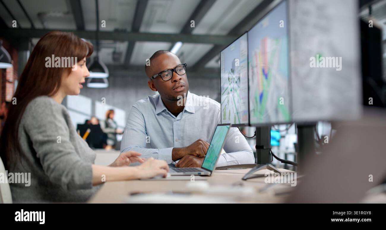 Young Professionals Analyze Urban Traffic Flow Using Digital Mapping And Design Software. Two Engineers Collaborate Stock Photo