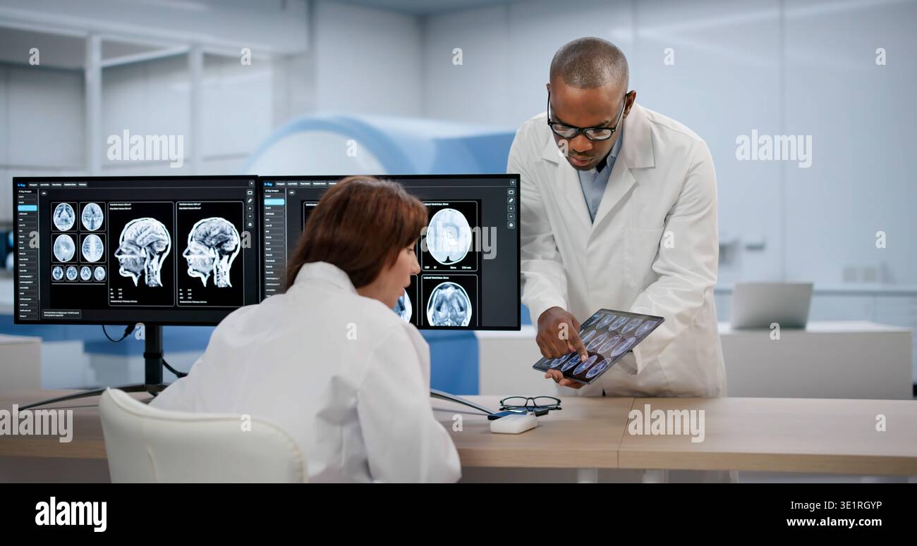 Two Medical Technicians Carefully Study Brain MRI Scans Together Using Computers. A Neurologist Stock Photo