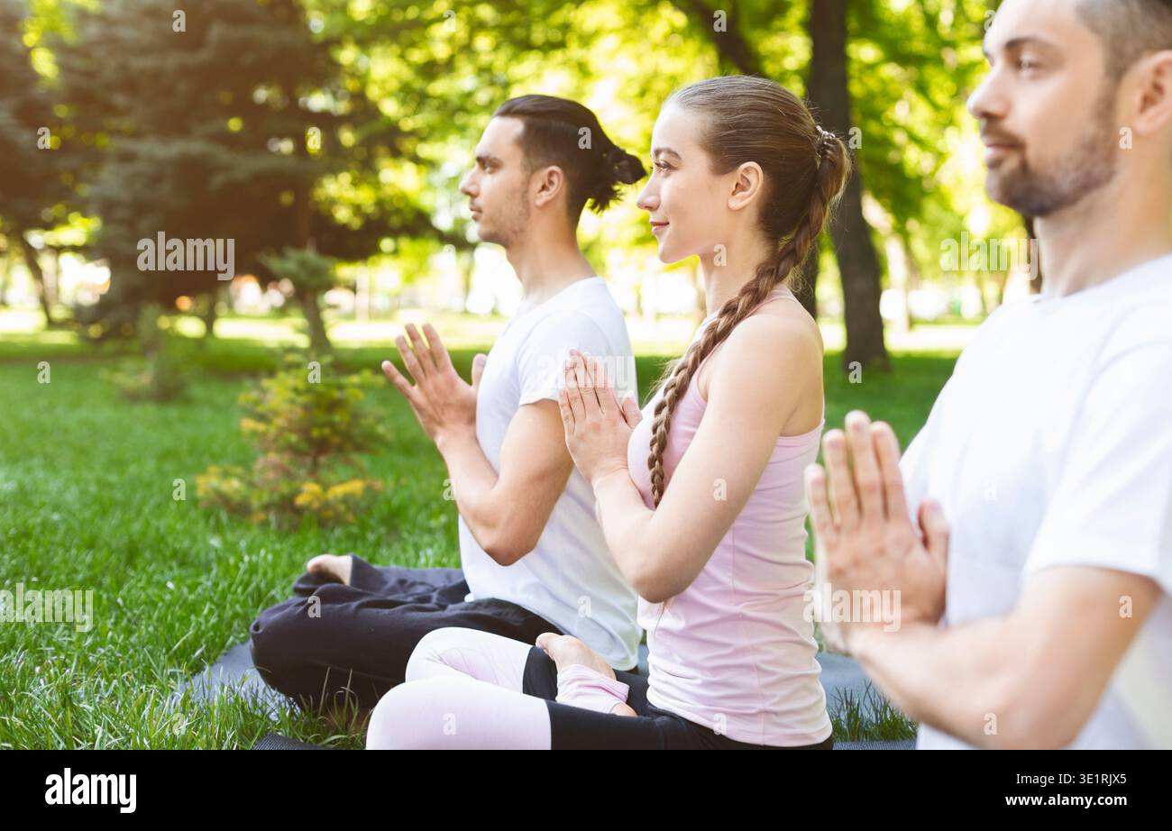 Three friends holding hands in namaste while practicing yoga outdoors Stock Photo