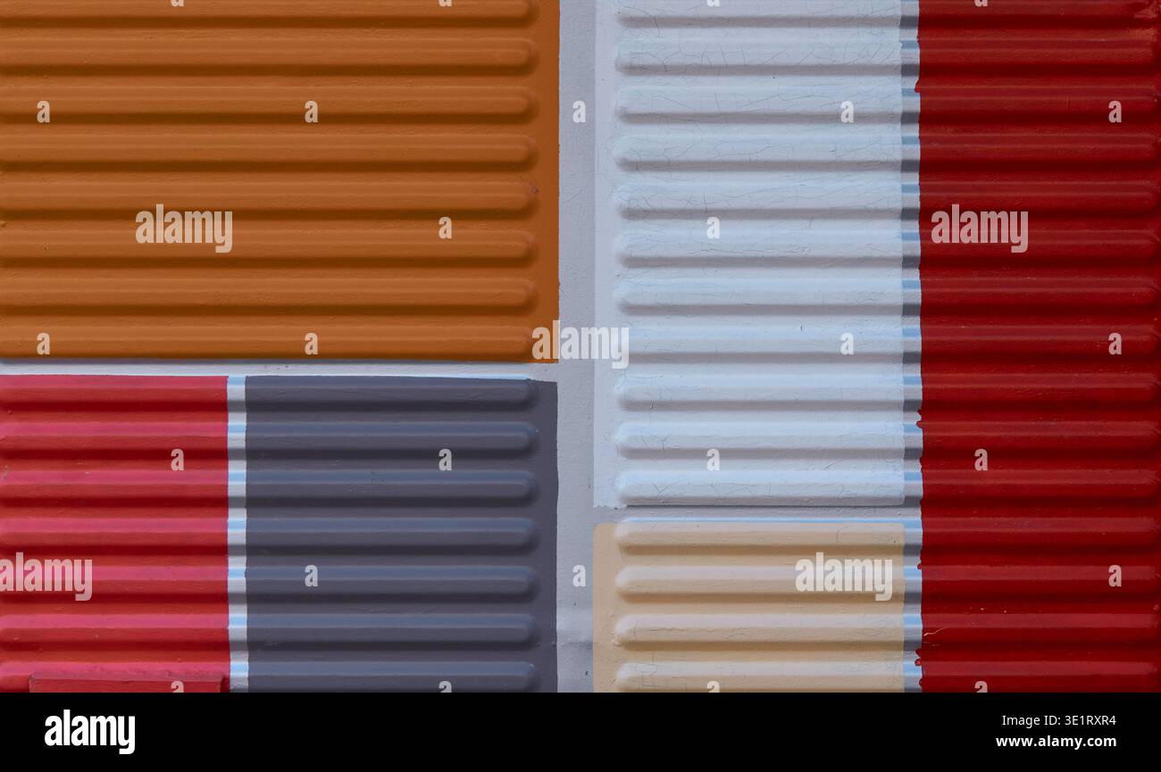 A texture of multi-colored ribbed metal siding with sections in orange, red, gray, white, and beige arranged in a geometric layout Stock Photo