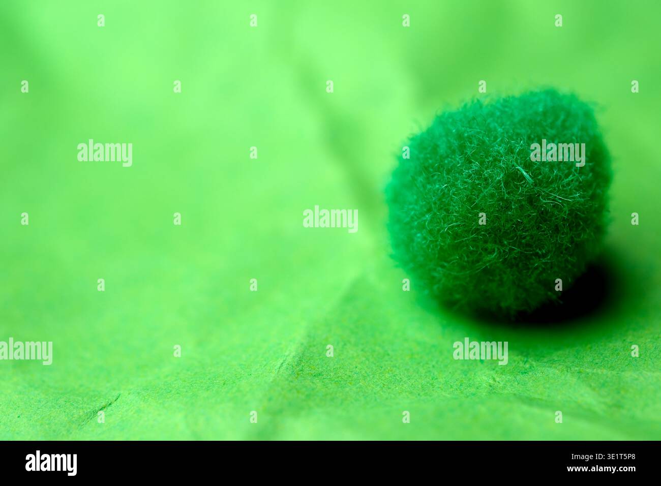 A small, fuzzy green ball sits on crumpled green paper, glowing softly in the light. Stock Photo