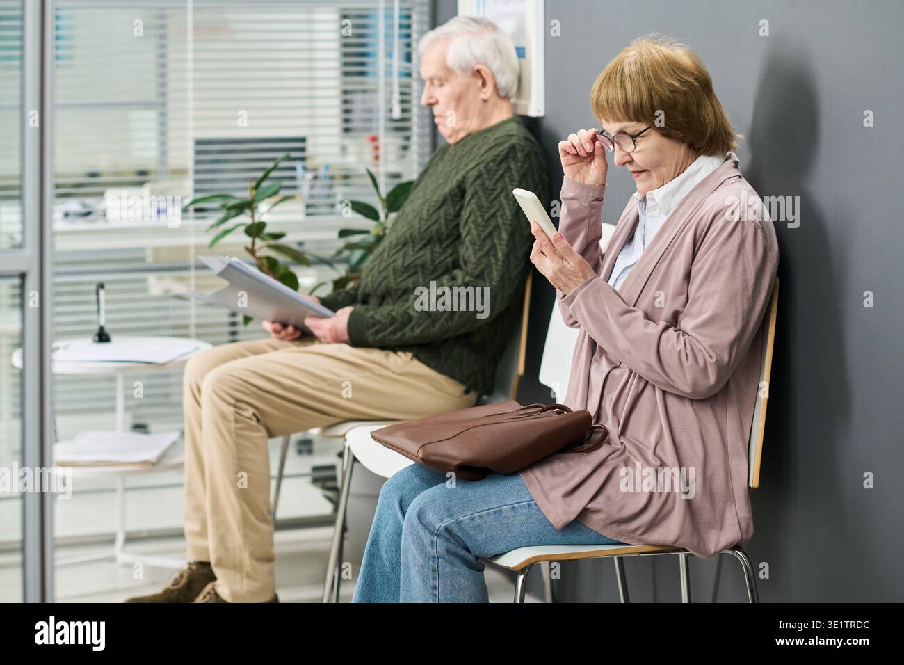 Senior Woman Using Smartphone While Senior Man Reading Documents Stock Photo