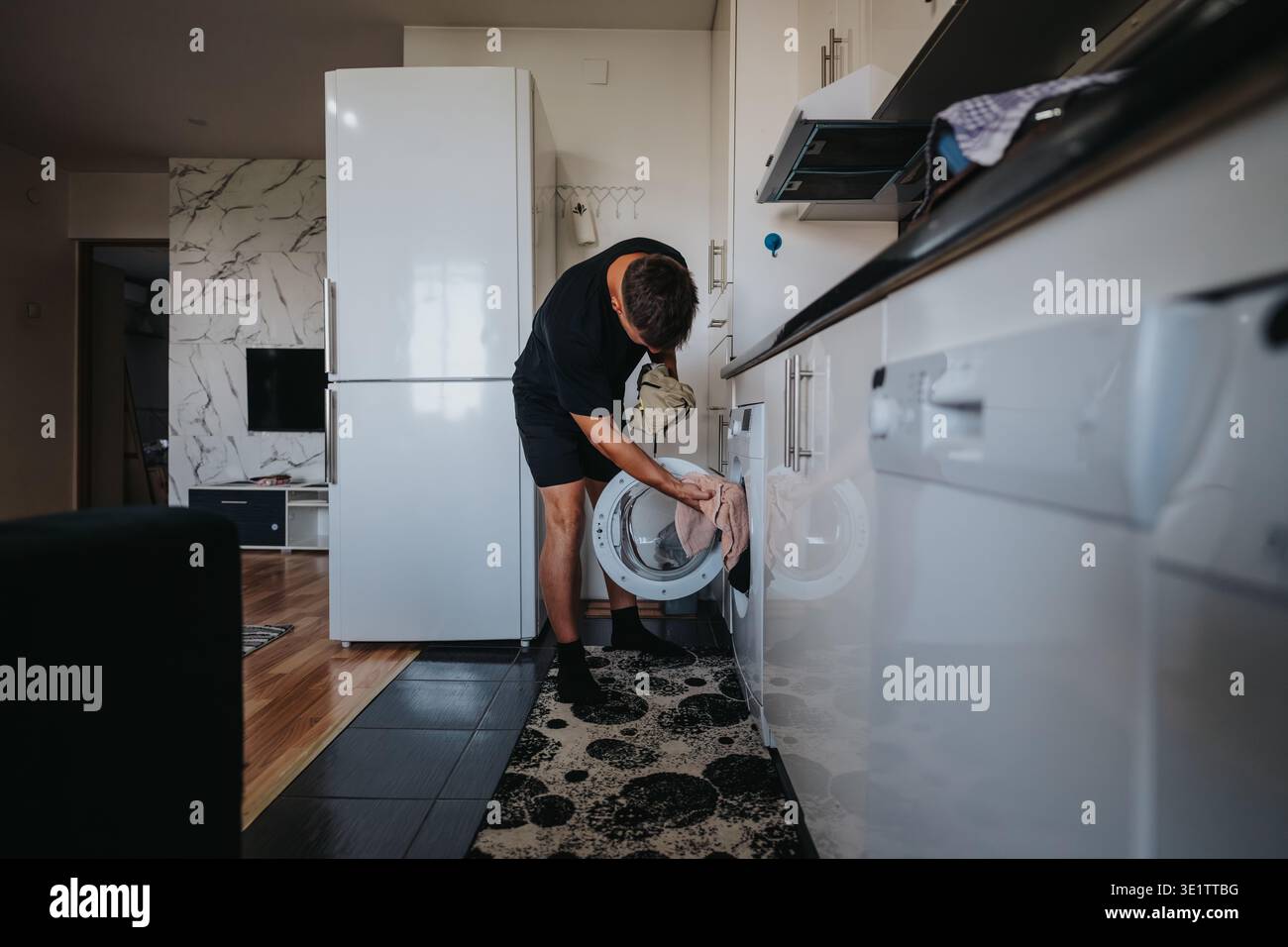 Man doing laundry at home loading a front-load washing machine in a modern kitchen Stock Photo