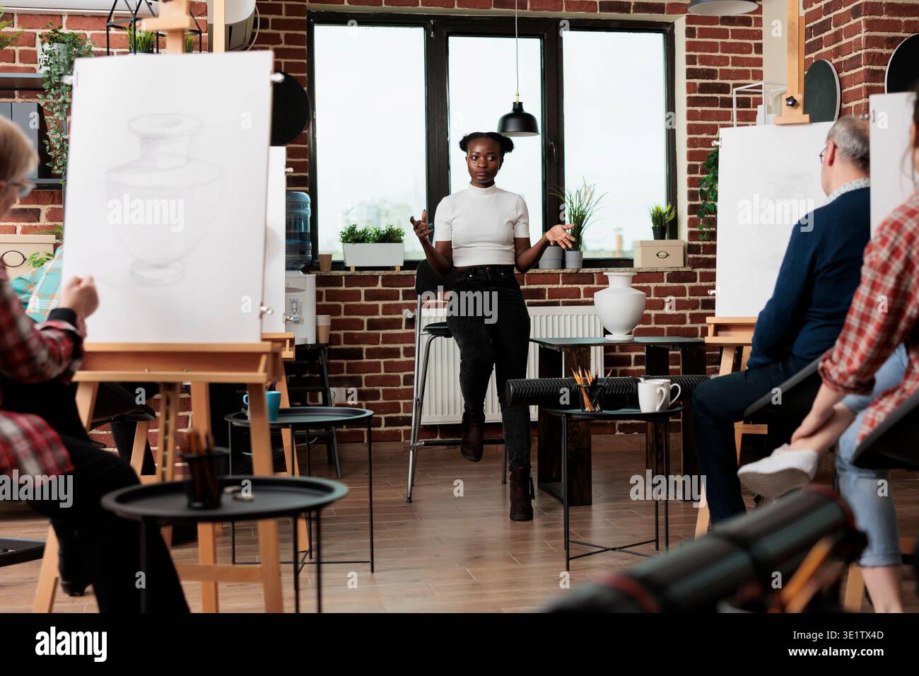 Art classes for adults. Group of different aged people attending drawing workshop, picking up new skills. Students sitting at easels in classroom and listening to instructor, learn to draw Stock Photo