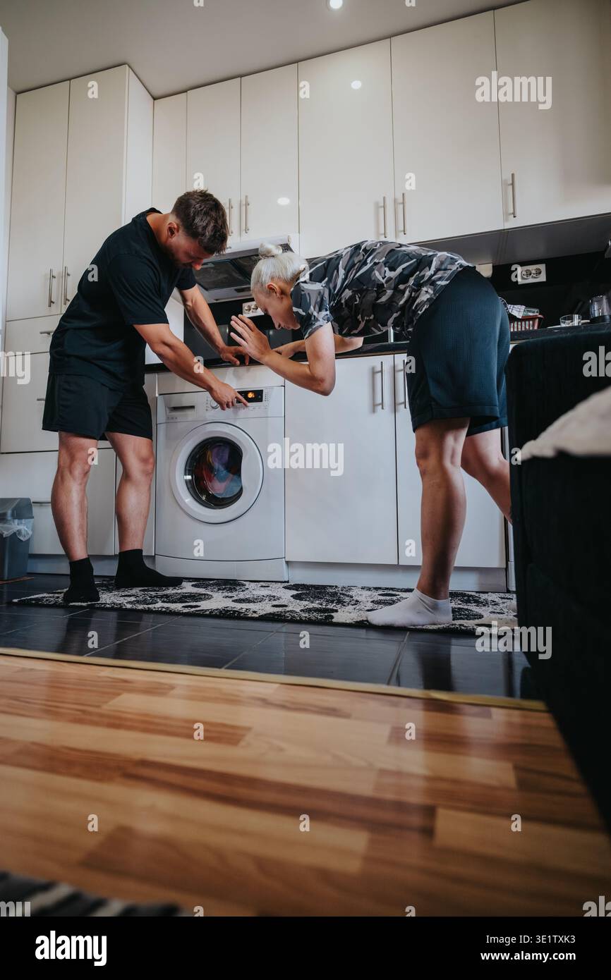 Young couple checking a front-load washing machine while doing laundry in their kitchen at home Stock Photo