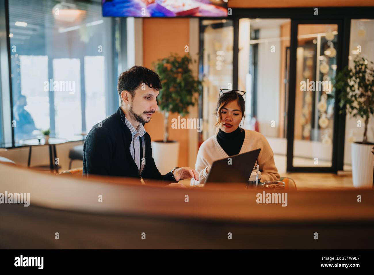 Business coworkers discussing project ideas over a laptop in a modern office lounge Stock Photo