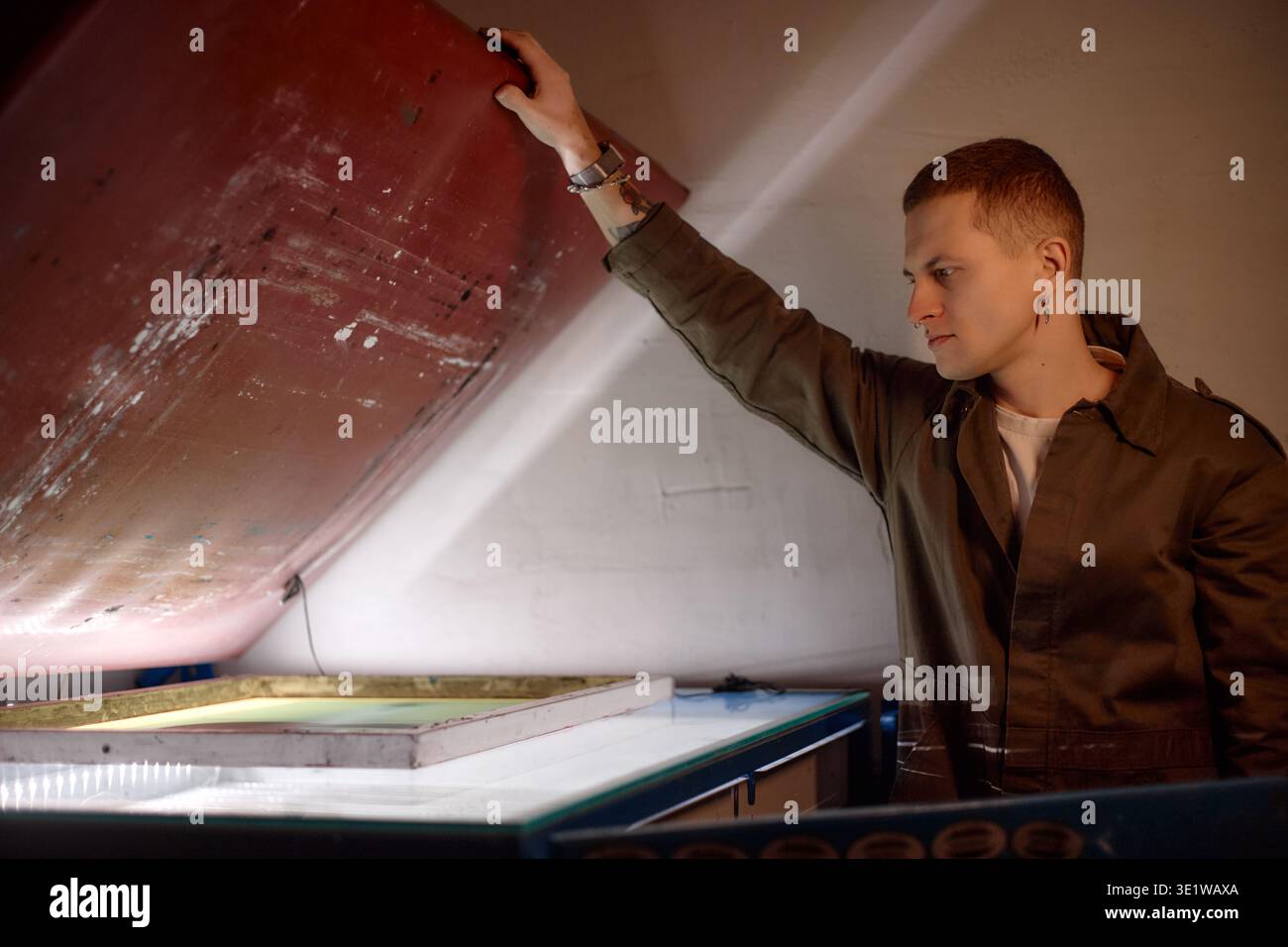 Young Man Operating Industrial Screen Printing Equipment Indoors Stock Photo