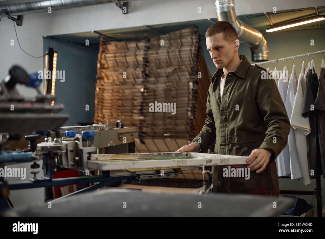 Young Man Operating Screen Printing Machine in Industrial Workshop Stock Photo