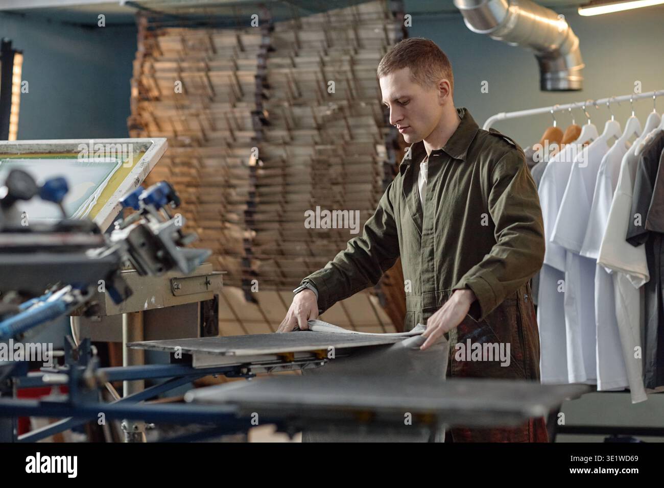 Young Man Operating Screen Printing Machine in Clothing Workshop Stock Photo