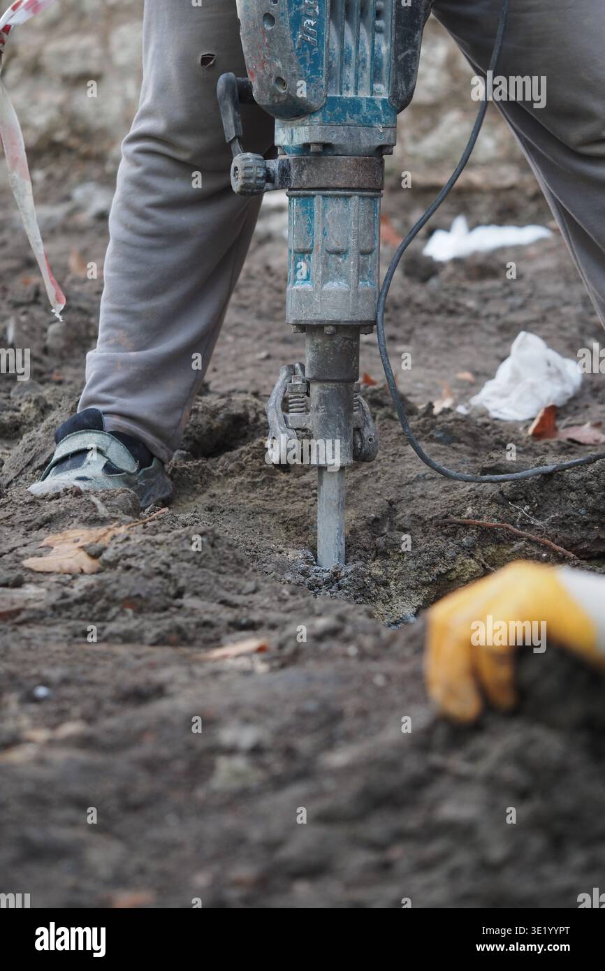 Construction worker uses jackhammer on ground surface Stock Photo