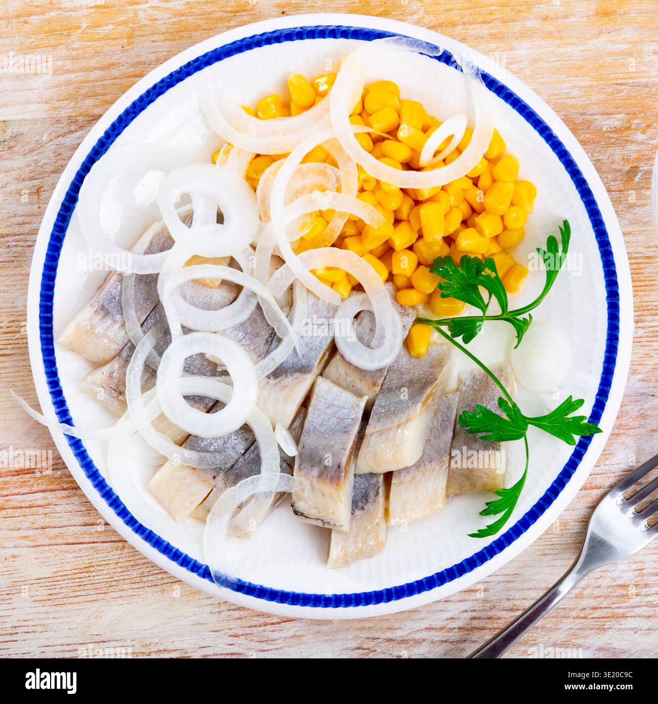 Sliced pickled herring fillet with corn and onions on plate Stock Photo