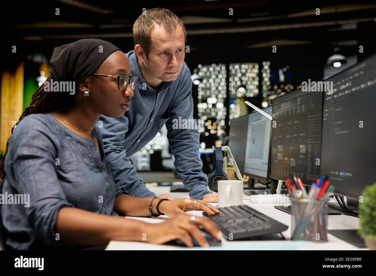 Manager supervising intern in startup office coding advanced machine learning models enhancing automation. Silicon Valley workplace team leader and teaching trainee to use AI on computer at desk Stock Photo