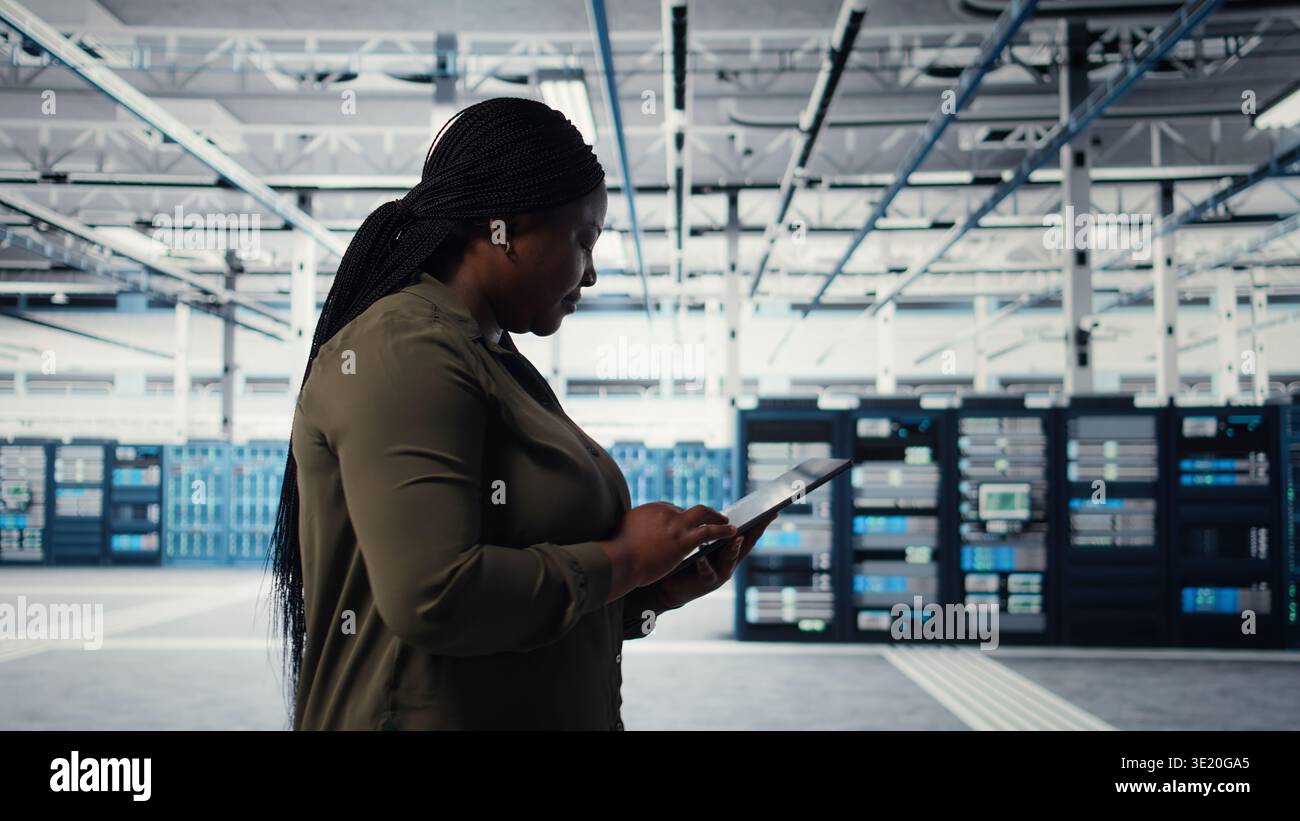 Developer in data center using tablet to upgrade systems for increase in clients workload capacity. IT expert in server farm configuring hardware, improving data processing speed, camera A Stock Photo