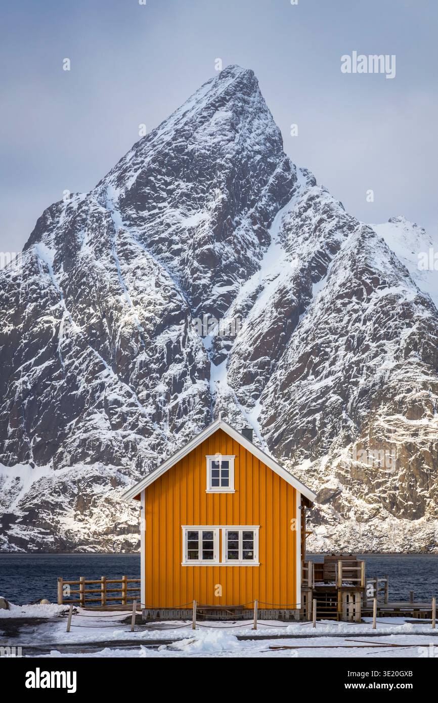 View of the Famous Yellow House with view of Olstind peak covered with snow in the background. Sakrisoy, Reine, Nordland, Lofoten Islands, Norway. Stock Photo