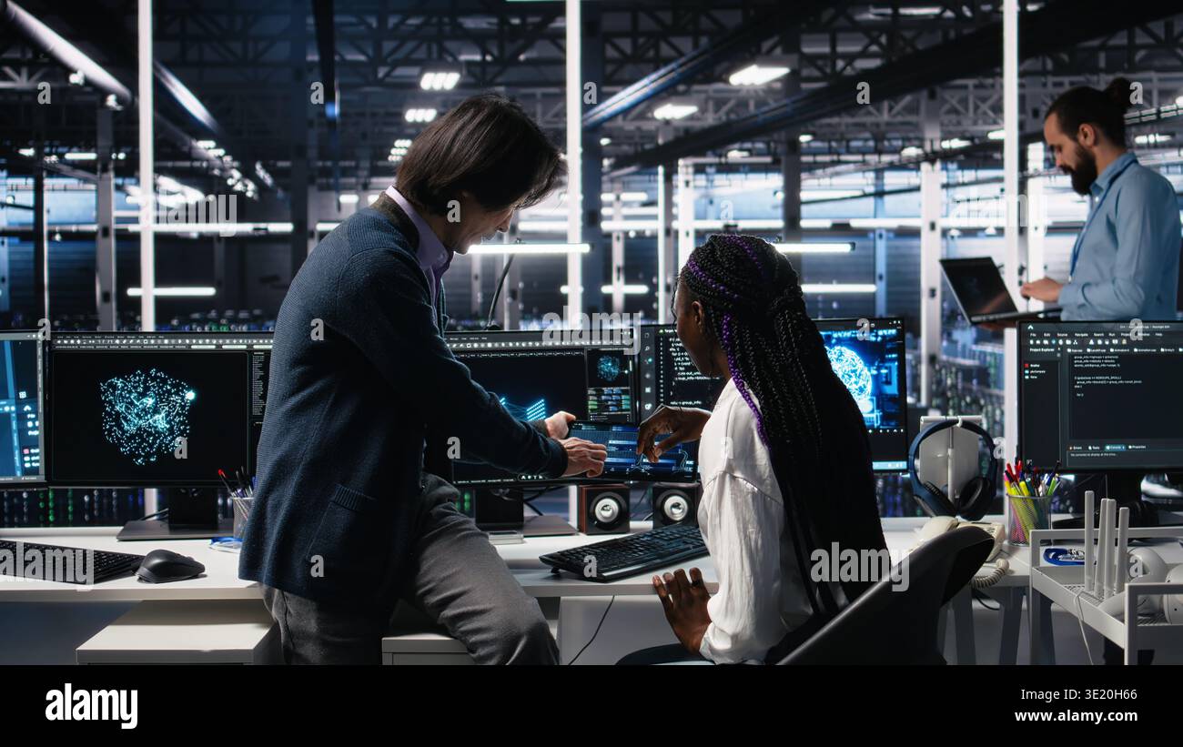 Senior engineer and trainee in data center working on neural network software development. Lead programmer and intern in server room implementing machine learning technology using PC, camera A Stock Photo