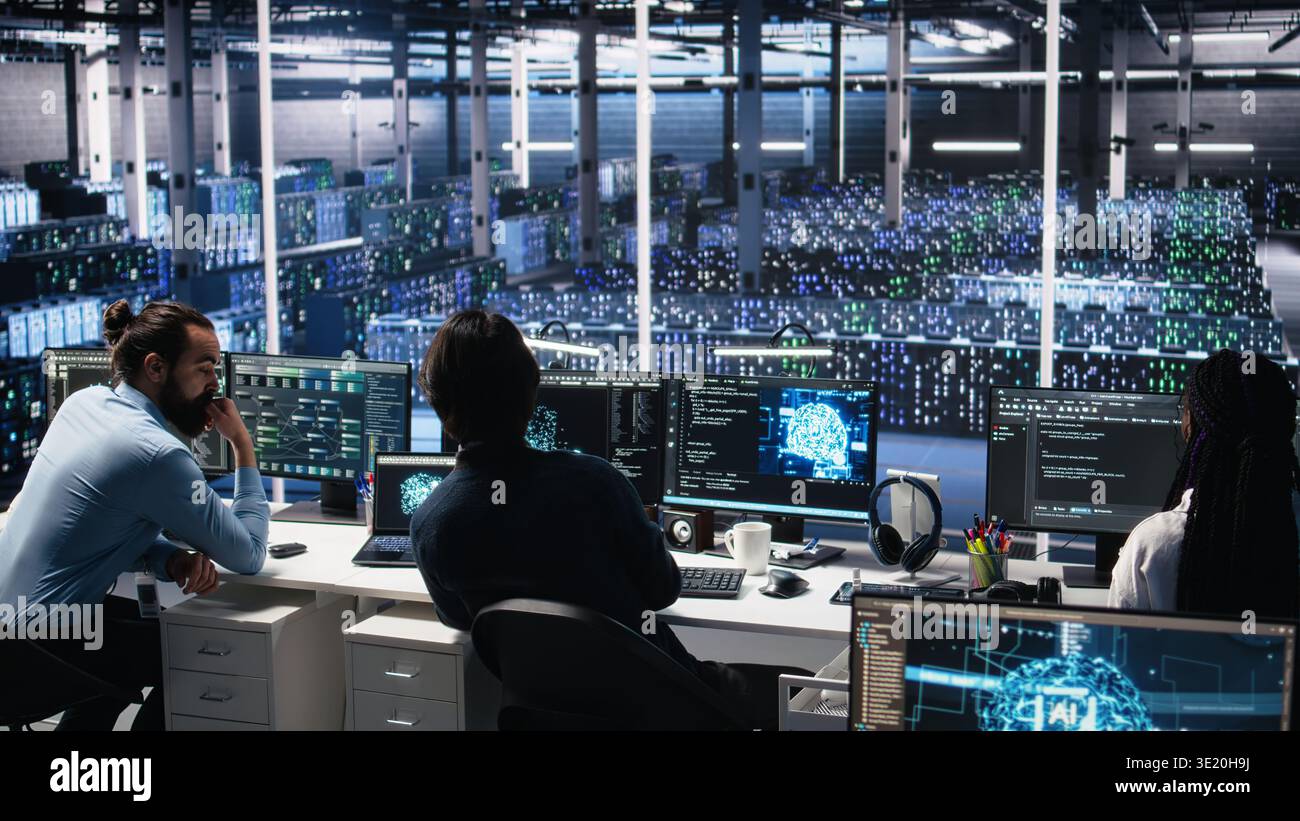 Server room system administrators using AI to review infrastructure diagnostics. IT professionals in data center analyzing performance data using artificial intelligence technology, camera A Stock Photo