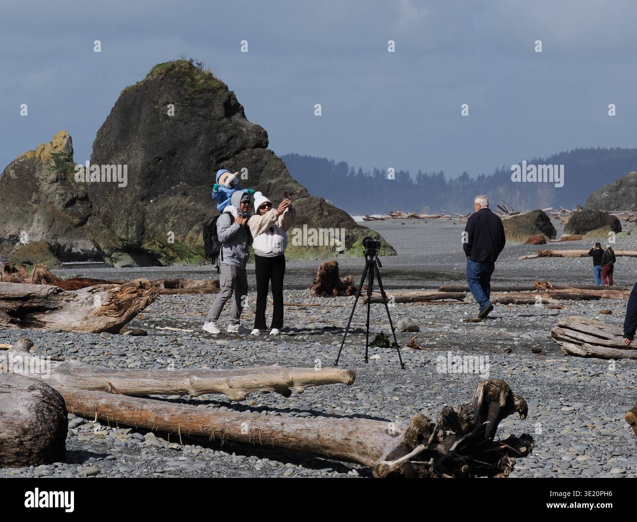 A young family pose for a selfie on Ruby Beach on the Pacific coast in Olympic National Park, Washington, USA, with driftwood and surf Stock Photo