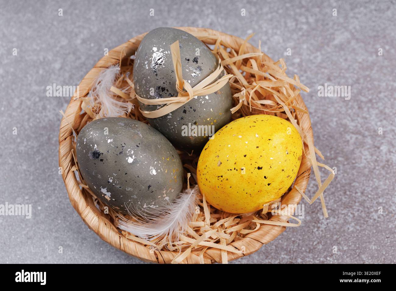Easter eggs in wicker basket with yellow egg and feathers Stock Photo
