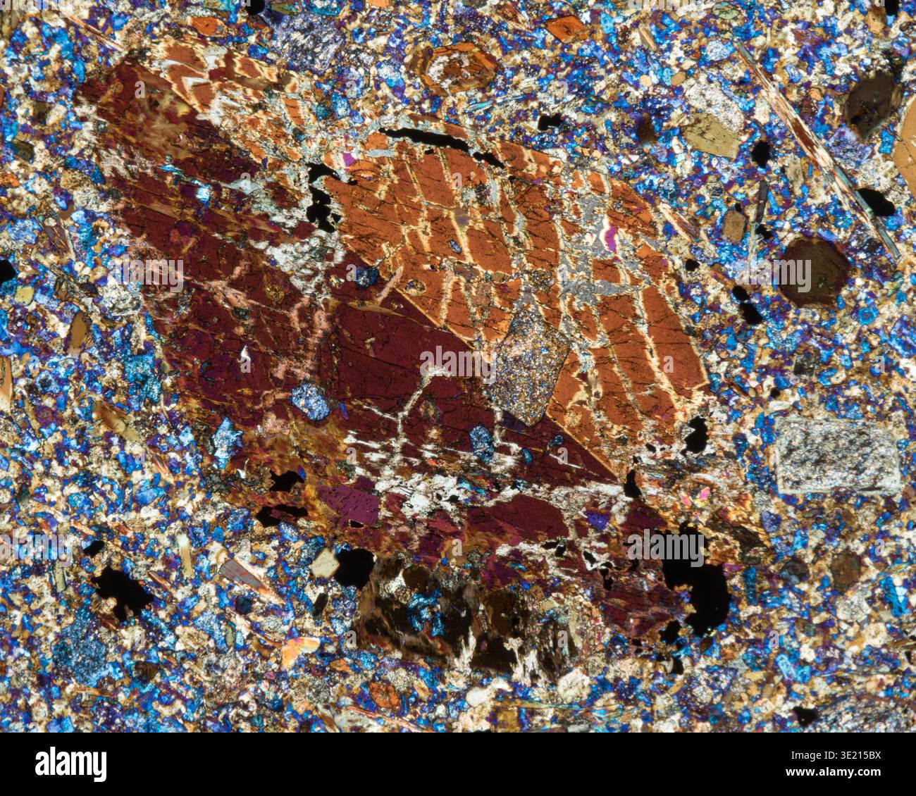 Polarised light micrograph of a sample of basalt from the Ulten Valley, South Tyrol, Italy. Basalt is formed when the earth's mantle melts. The thin, low-silica magma cools relatively quickly when released to the Earth's surface or ocean. The magma usually contains inclusions (xenocryst) of minerals or entire rocks (xenolite) with a higher melting point, which were carried along during the ascent. Basalt consists mainly of a mixture of iron and magnesium silicates with pyroxene and calcium-rich feldspar (plagioclase) and also olivine. Magnification: x60 when printed at 15 centimetres wide. Stock Photo