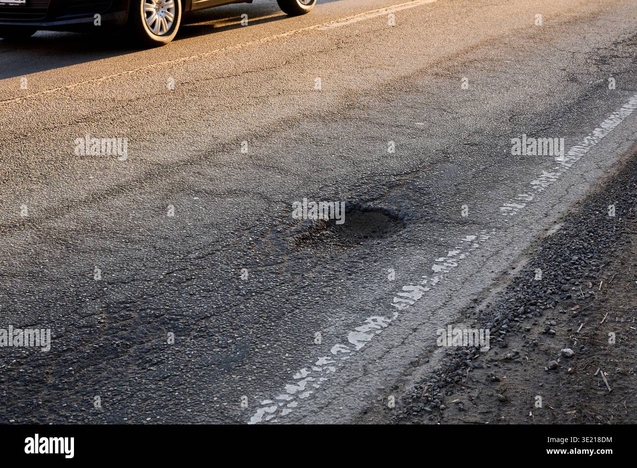 Deep Pothole A prominent and deep pothole severely damages a worn asphalt road ...