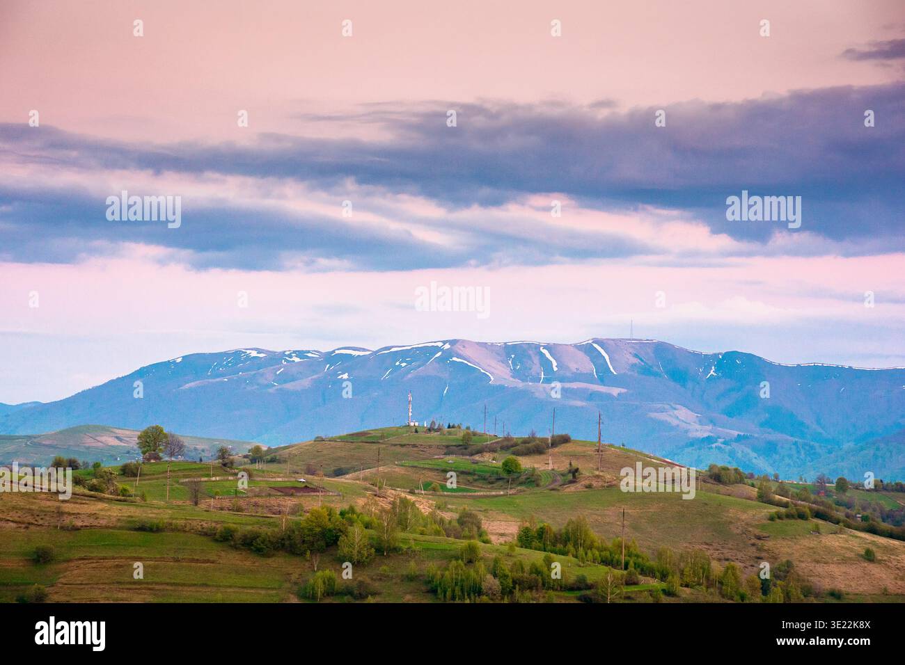 dusk over mountainous countryside scenery. dramatic sky above the distant valley and ridge. remote green meadows and trees on rolling hills. beautiful Stock Photo