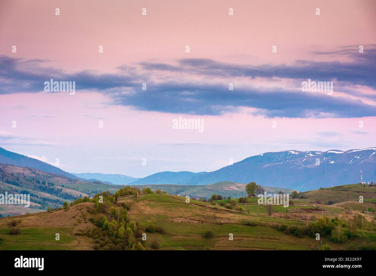dusk over mountainous countryside scenery. dramatic sky above the distant valley and ridge. remote green meadows and trees on rolling hills. beautiful Stock Photo