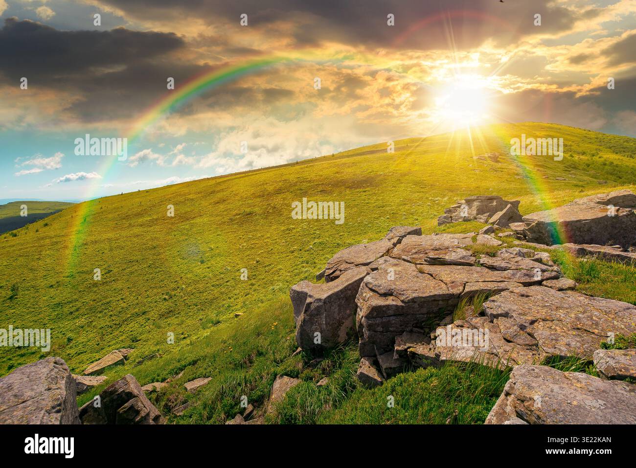 sunset over rocks and rolling hills in mountain landscape in summer. scenery with green grass on alpine meadow under sky with clouds. background for r Stock Photo
