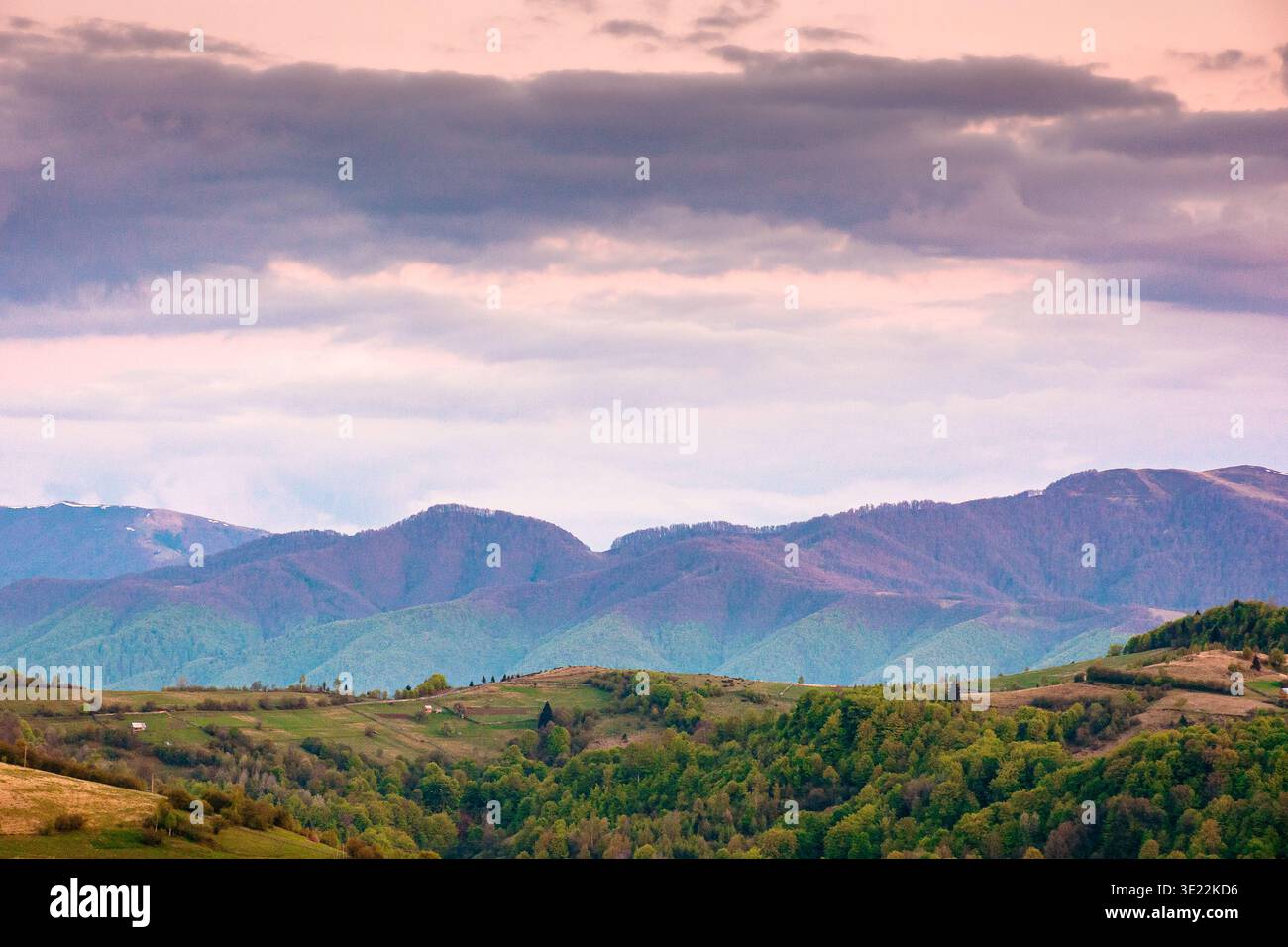dusk over mountainous countryside scenery. dramatic sky above the distant valley and ridge. remote green meadows and trees on rolling hills. beautiful Stock Photo