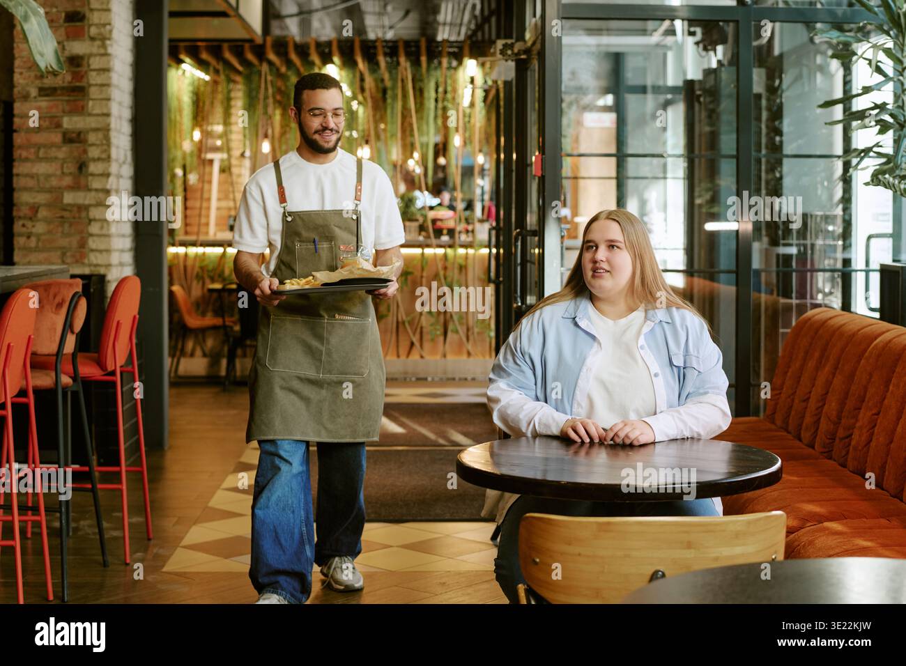Young Woman Waiting While Young Man Serving Food in Modern Cafe Stock Photo