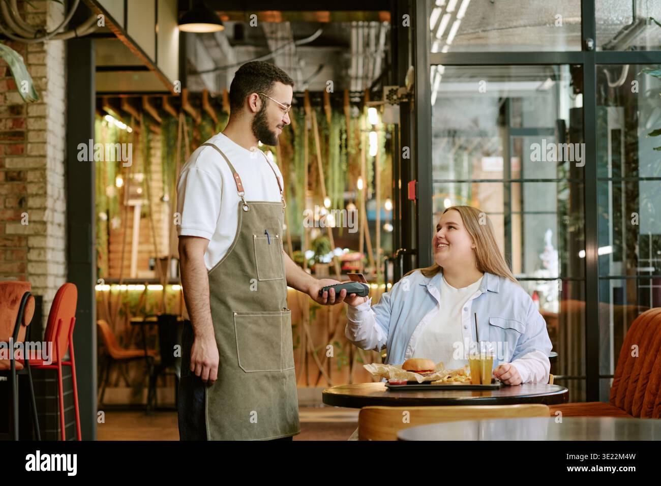Young Woman Paying Bill to Middle Aged Man Waiter in Cafe Stock Photo