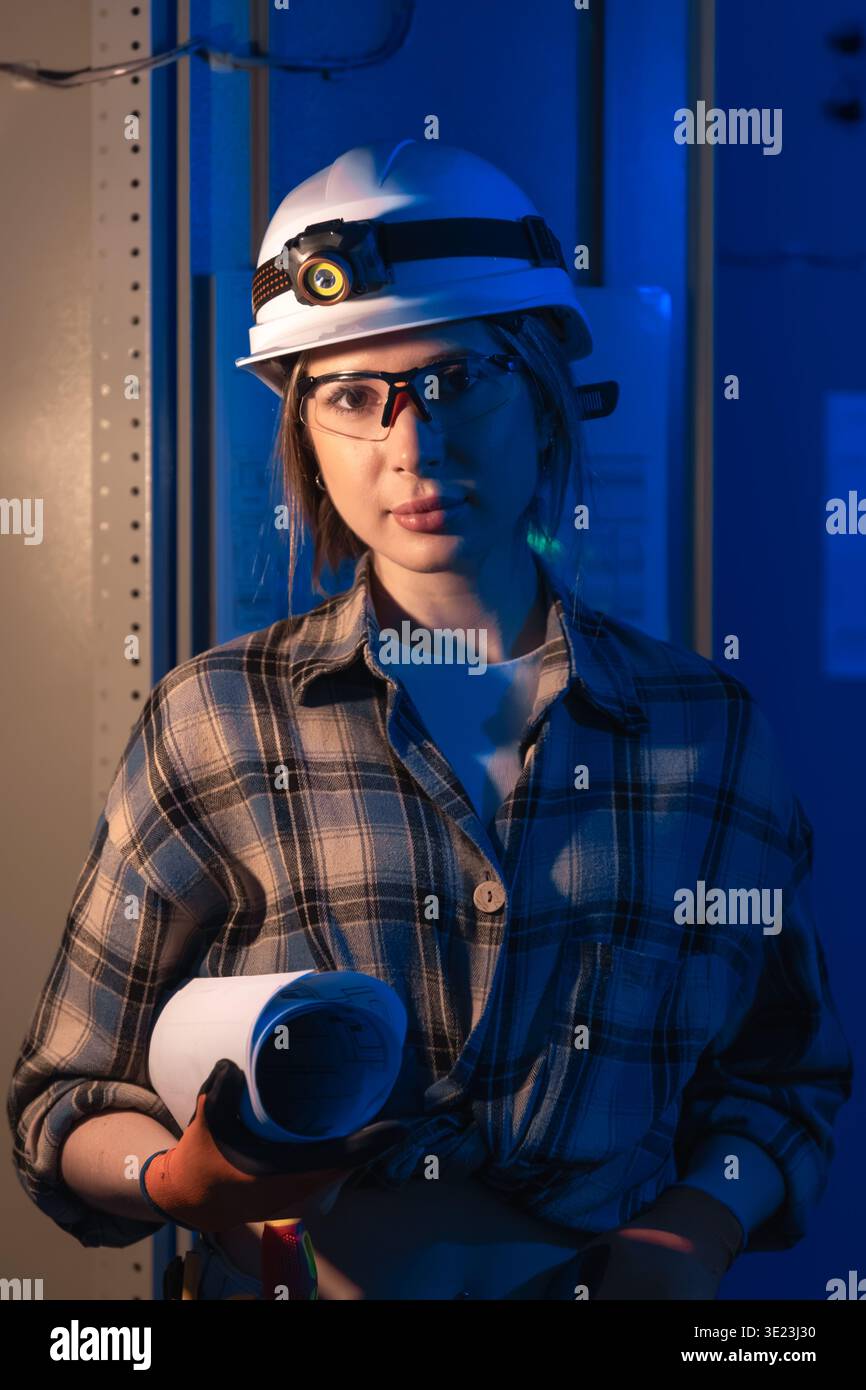 Electrical engineer holding system blueprint near industrial switchboard. Engineering portrait. Stock Photo