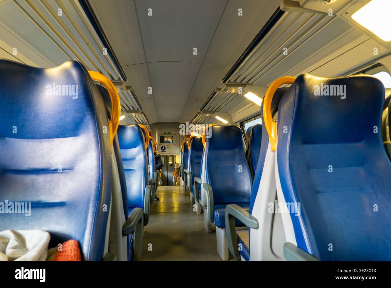 The perspective shot shows rows of empty blue passenger seats with yellow grab handles in a clean train compartment, illuminated by overhead lights Stock Photo