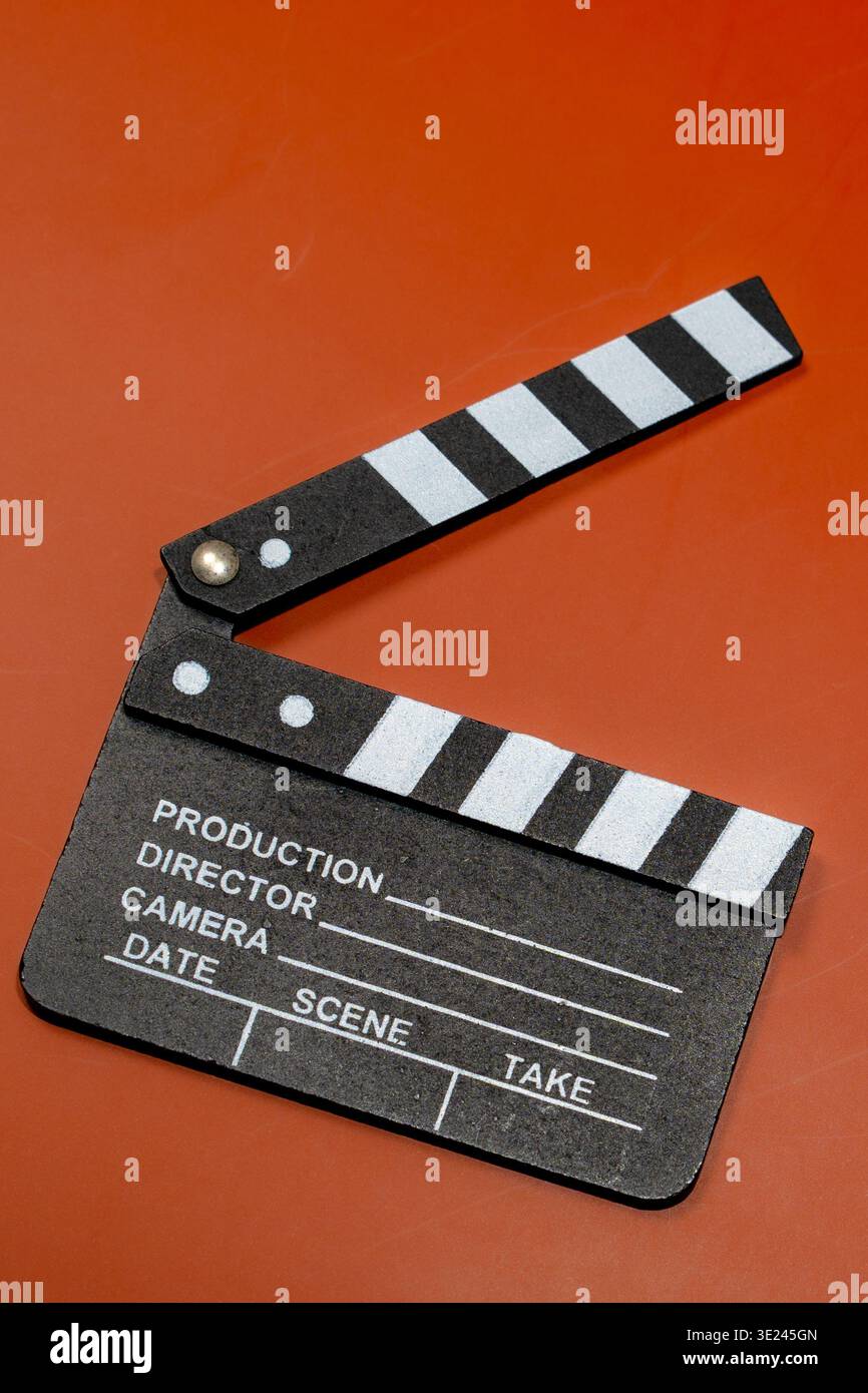 A classic clapperboard sits on a contrasting orange surface, ready for the next scene to be filmed. Stock Photo