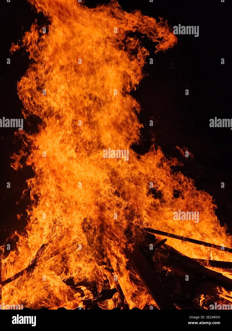 Bright orange flames leap and dance in a roaring fire, capturing the warmth, intensity, and dynamic energy of burning wood or a bonfire. Stock Photo