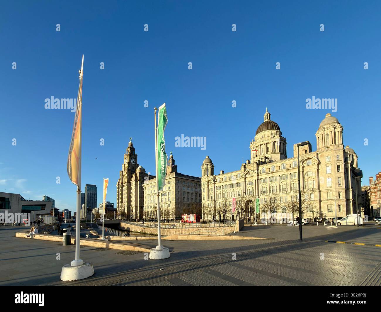 The three Graces and welcome to Liverpool flags at Pier Head on a sunny spring day - Smartphone Captured Stock Image