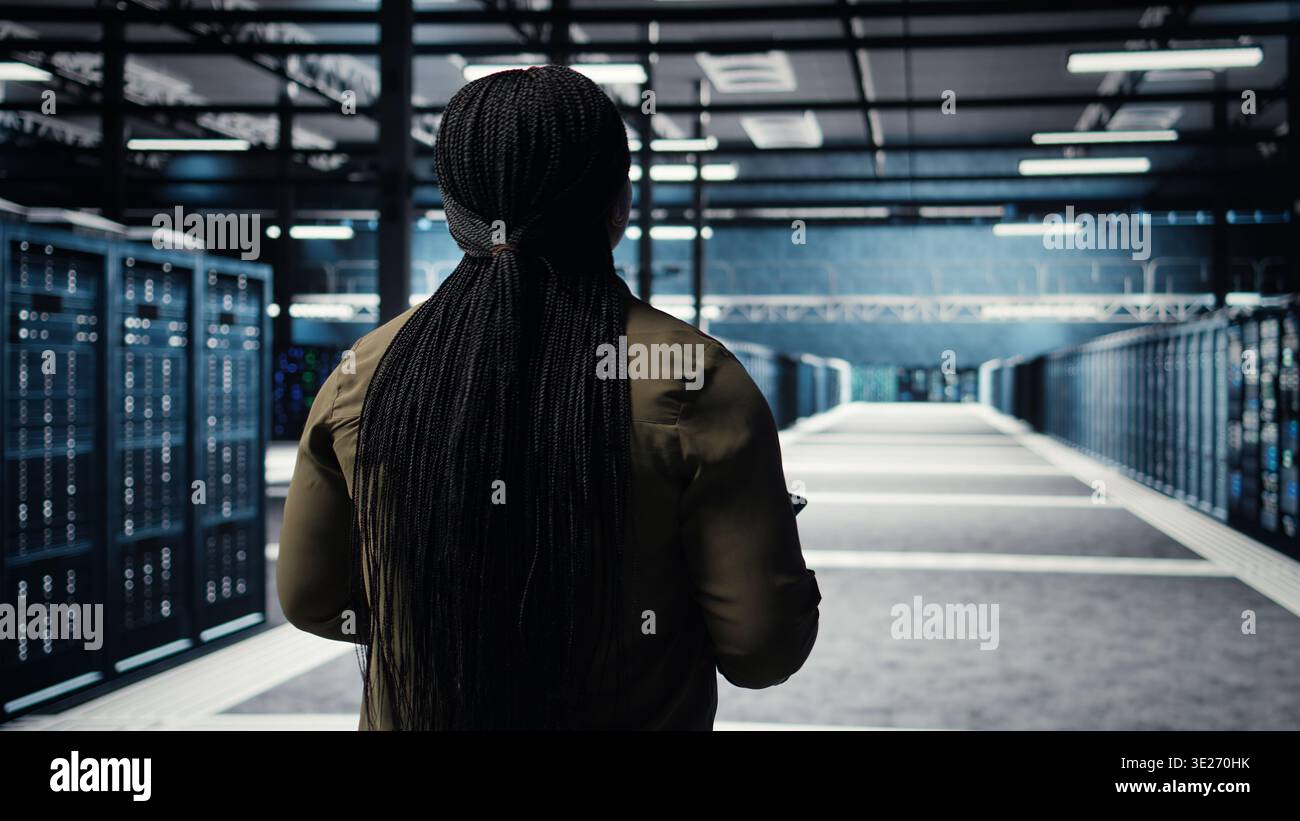 Data center system administrator monitors data center metrics on tablet to enhance operational effectiveness. IT expert in server room using analytics program to predict performance, camera A Stock Photo