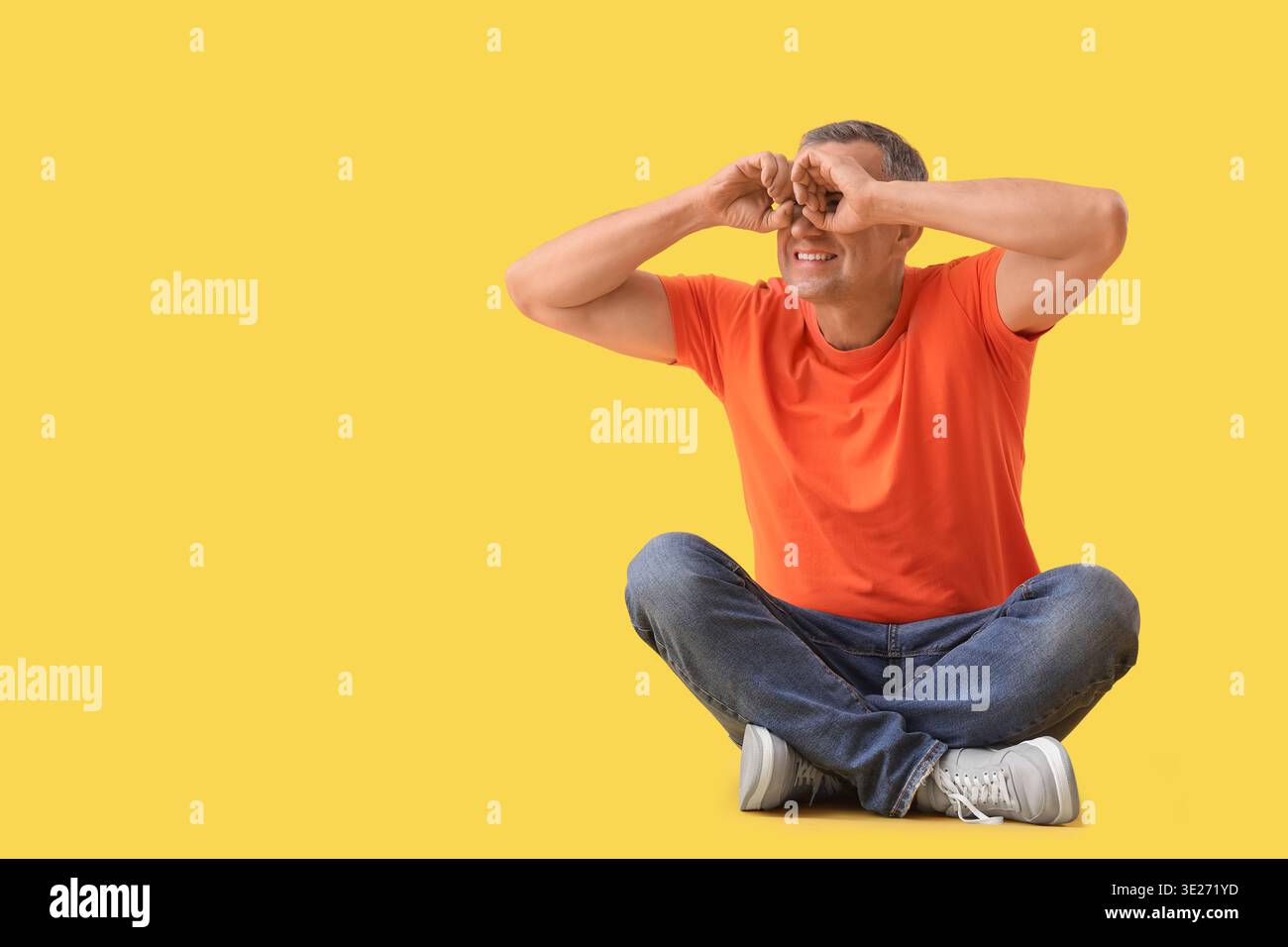 Mature man looking through imaginary binoculars on yellow background Stock Photo