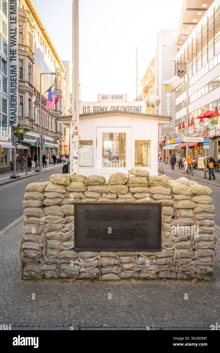 Checkpoint Charlie is a famous location in Berlin. It includes a small booth and a wall made of sandbags. Many shops and buildings surround it. Visitors explore this area daily. Stock Photo