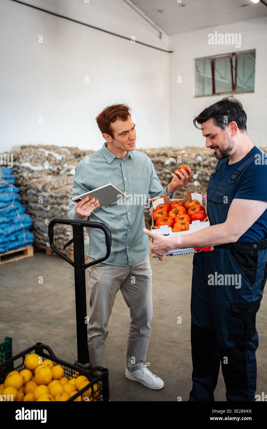 Warehouse workers discussing produce quality holding fresh tomatoes Stock Photo