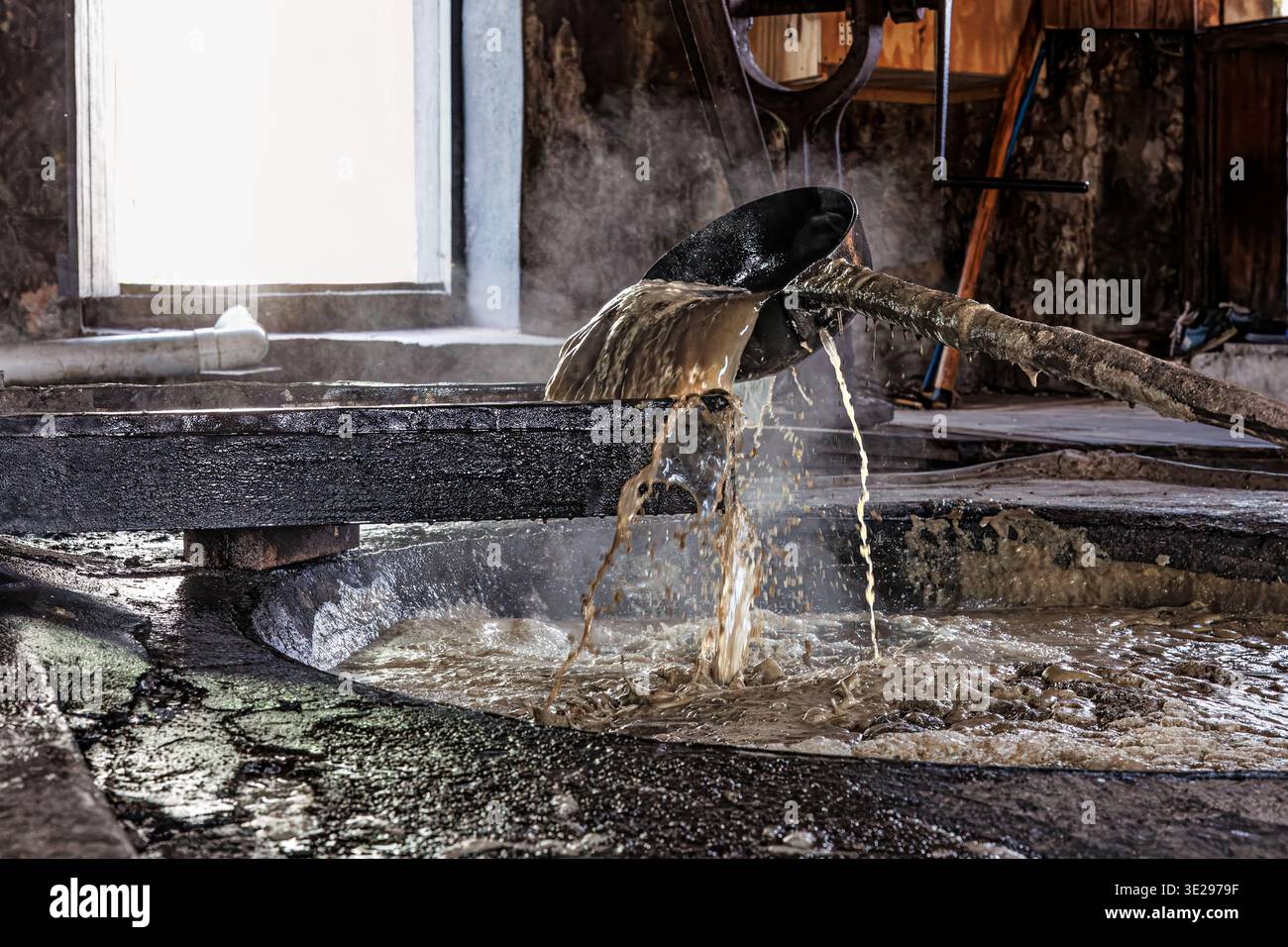 Traditional method to tansfer from cooler to hotter pan to reduce the sugar cane juice by heating, River Antoine Rum Distillery, St Patrick parish, Gr Stock Photo